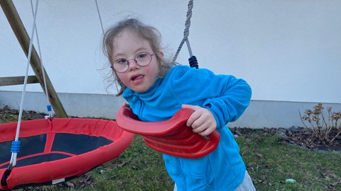 Nora aus Kruft ist sieben Jahre alt und hat das Down-Syndrom. Sie spielt gerne im Garten, etwa auf der Schaukel. 