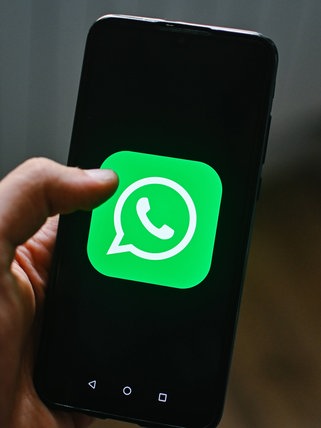 Eine männliche Hand hält ein Handy mit dem grünen Logo von WhatsApp auf dem Display