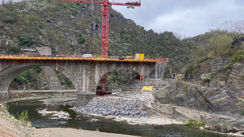 Überall wird gebaut im Ahrtal. Zum Beispiel in Altenahr unterhalb der Burgruine Are, wo die Deutsche Bahn einen Viadukt für die Ahrtalbahn wiederaufbaut und der Landesmobilität eine Brücke für den Ahrtal-Radweg. Touristen beobachten die Bauarbeiten.