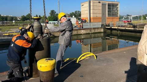 Zwei Männer arbeiten an einer Schleuse und ziehen an einem großen Metallteil.