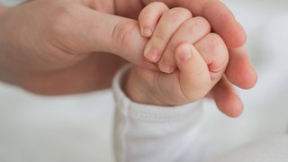 Symbolbild: Die Hand eines Neugeborenen umfasst den Daumen der Mutter.