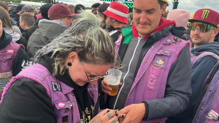Frau lackiert einem Mann bei Rock Ring die Nägel schwarz.