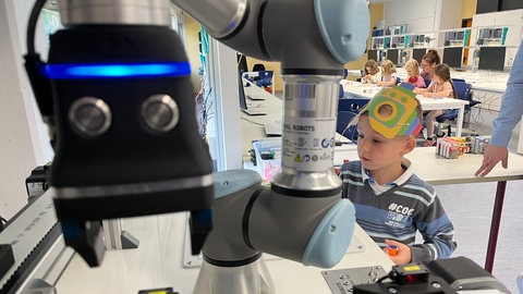 Im Industrielabor 4.0 in der Carl-Benz-Schule Koblenz steht ein Junge im Vorschulalter vor einem Roboterarm, den er per Knopfdruck bedient.