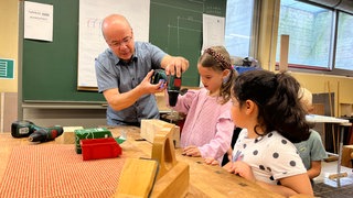 Ein Berufsschullehrer der Carl-Benz-Schule Koblenz zeigt zwei Mädchen im Kindergartenalter, wie man einen Akkuschrauber bedient.