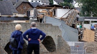 Zwei Menschen schauen sich das Ausmaß der Flutkatastrophe im Ahrtal an. Flutbetroffene werden auch in den kommenden Jahren von der ISB beraten in einem neuen Angebot.