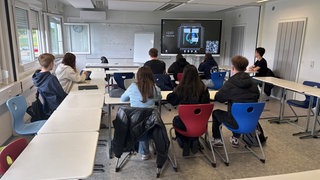 Schülerinnen und Schüler sitzen wie die Sardinen in einer Blechbüchse, in einem provisorischen Klassenraum, des Are-Gymnasiums, der recht eng ist. 