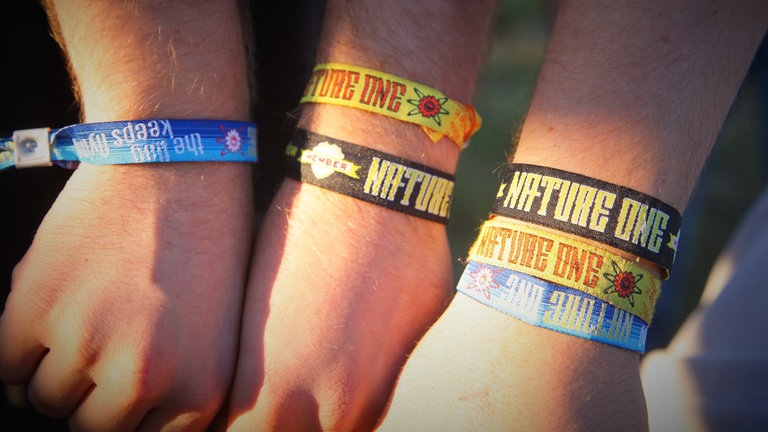 Drei Besucher der Nature One 2010 zeigen ihre Festivalbändchen