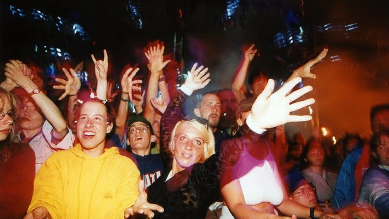 1998 hatten sieben Clubs erstmals eigene Tanzbereiche auf dem Festivalgelände der Nature One. Auf dem Bild sind feierende Besucherinnen und Besucher zu sehen.