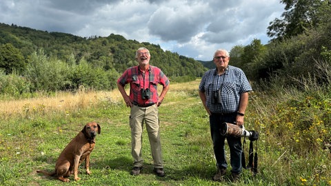 Storchexperte Jürgen Wagner steht zusammen mit Naturfotograf Michael Andres auf einer Wiese im Ahrtal. Sie sind auf der Suche nach Schwarzstörchen.