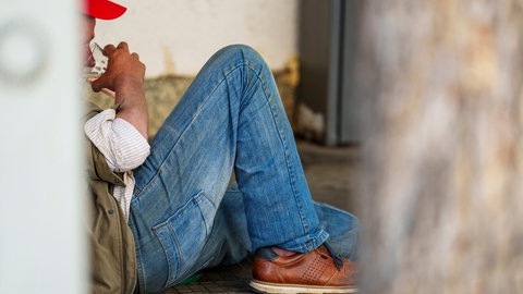 Obdachloser Mann trinkt im Schatten ein Glas Wasser, während einer Hitzewelle.
