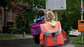 Der Bus kommt nicht: Schulkinder stehen an einer leeren Haltestelle und schauen auf den Fahrplan.