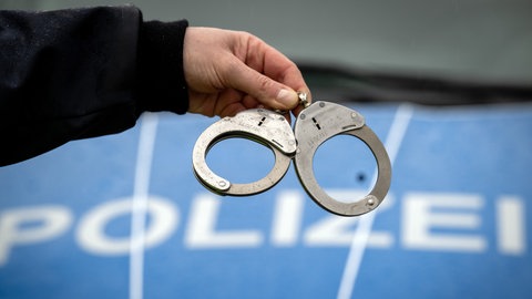 Handschellen vor einem Polizeiwagen - mehrere Festnahme wegen Callcenterbetrug