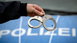 Handschellen vor einem Polizeiwagen - mehrere Festnahme wegen Callcenterbetrug