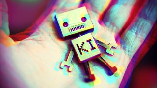Roboter mit Aufschrift KI liegt auf einer menschlichen Hand. 