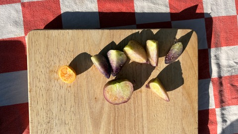 Eine aufgeschnittene Physalis auf einem Holzbrett und daneben mehrere aufgeschnittene Tomatillos, die aus Mexiko stammen.