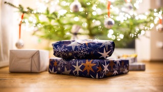Geschenke an einer mit Lichterketten und Weihnachtskugeln geschmückten Tanne