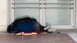 Ein Obdachloser Mann liegt auf der Straße (Symbolbild)