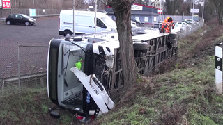 Ein schwer beschädigter Bus liegt auf die Seite gekippt in einem Graben. Er liegt zwischen der Leitplanke und einem Baum.