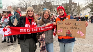Drei junge Frauen halten Plakate bei der Demo gegen die geplanten Kürzungen der Evangelische Kirche.