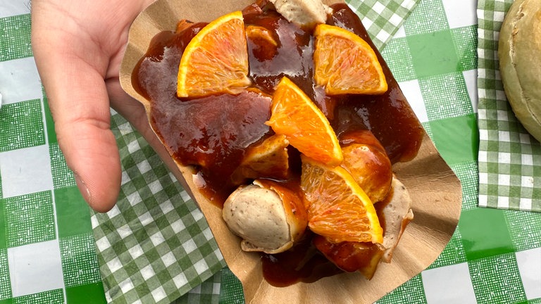 Ein Besucher des Currywurst-Festivals 2025 in Neuwied hält eine Currywurst im Schottland-Style mit Whiskeysoße und Orangen in der Hand. 
