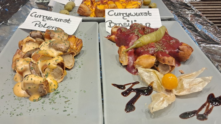 Zwei Currywürste mit jeweils unterschiedlicher Sauce auf Tellern nebeneinander: Beim Currywurstfestival 2026 in Neuwied kann man wieder unzählige Varianten probieren. 