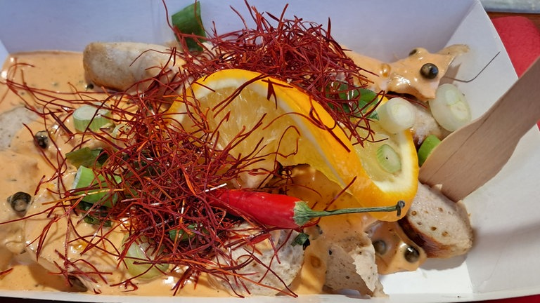 Eine Currywurst-Variante mit frischer Zitrone, roten Chilifäden und einer hellen Sauce: Beim Currywurstfestival 2026 kann man unterschiedlichste Saucen probieren.