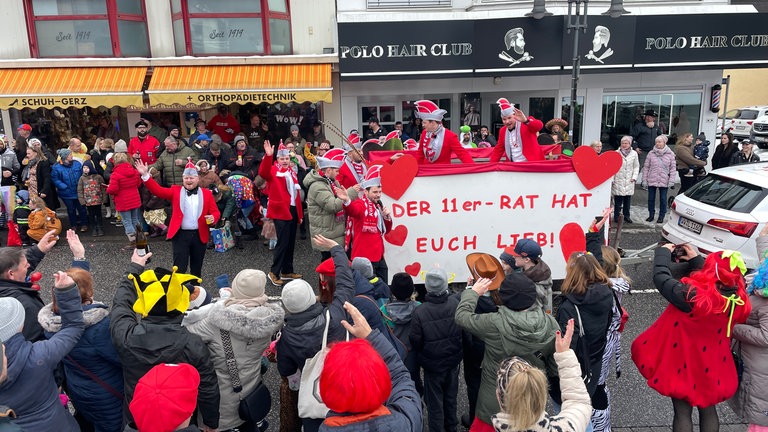 Das Foto zeigt den Elferrat beim Rosenmontagsumzug 2026 in Rennerod. Der Wagen hat ein Schild mit der Aufschrift "Der 11er-Rat hat euch lieb."