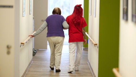 Eine Pflegekraft begleitet eine Seniorin durch den Flur. Das Verwaltungsgericht Koblenz hat jetzt ein Urteil gesprochen: Die umstrittenen Beiträge zur Pflegekammer Rheinland-Pfalz waren rechtswidrig.