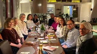 Mehrere Menschen sitzen an einem Tisch - vor ihnen liegen Bücher.