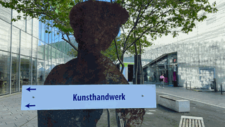 Ein Schild mit einer Messingfigur auf einem Platz in einer Stadt 