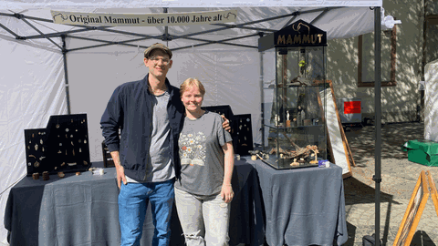 Ein junger Mann und eine Frau vor einem Schmuckstand auf einem Platz in einer Stadt 