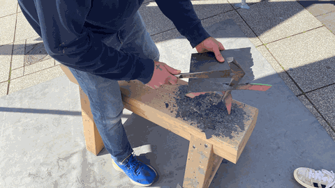 Ein Mann haut auf einem Holzblock eine Scheibe Schiefer in Form 
