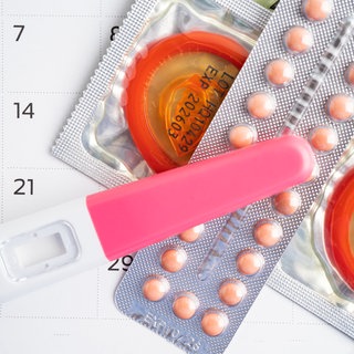 Schwangerschaftstest und Verhütungsmittel liegen auf einem Kalender