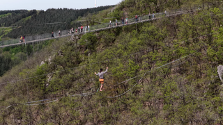 Ein mann geht auf einer Slackline dirket neben der Geierlay Hängeseilbrücke.