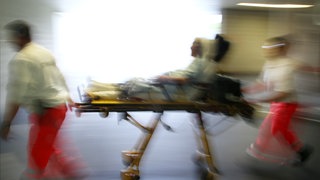 Rettungsassistenten liefern eine Notfallpatientin auf einer Trage in ein Krankenhaus ein.