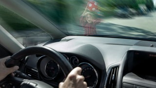 Auto fährt, Kind mit Ball vor Windschutzscheibe (Symbolbild)