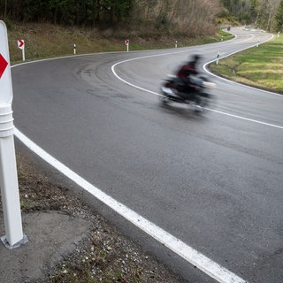 Ein Motorradfahrer fährt auf einer Landstraße und ist unscharf zu sehen, da er schnell fährt.