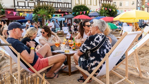 Eine Gruppe Menschen sitzt mit einem Getränk in Liegestühlen auf dem künstlich aufgeschütteten Sandstrand in der Altstadt von Linz am Rhein.