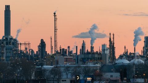 Rauchende Schornsteine der BASF in Ludwigshafen vor rötlichem Himmel.