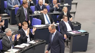 Friedrich Merz, CDU-Bundesvorsitzender und CDUCSU-Fraktionsvorsitzender im Bundestag, läuft an der AfD-Fraktion (rechts) vorbei, die nach der Bekanntgabe der Ergebnisse der Abstimmung für eine Verschärfung der Migrationspolitik reagiert.