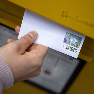 Eine Hand wirft einen Brief in einen gelben Post-Briefkasten. Fünf Bandenmitglieder stehen wegen Betrugs mit geklauten Rechnungen im Februar vor Gericht. 