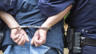 Ein Mann wird in Handschellen von Polizisten abgeführt. Symbolbild: Häftling aus dem Gefängnis Schifferstadt wurde von fünf Komplizen gewaltsam befreit
