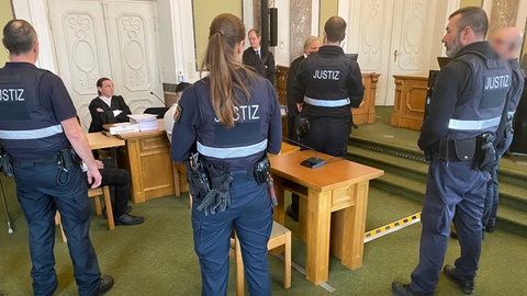 Justizbeamte sichern vor dem Prozessauftakt zu Postraub und Betrug am Landgericht Landau den Gerichtssaal. Den Angeklagten wird vorgeworfen, Rechnungen gestohlen und mit ihrer eigenen Kontonummer versehen zu haben.