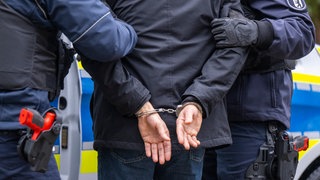 Polizisten führen einen Mann in Handschellen ab. Symbolbild. Mutmaßlicher Vergewaltiger in Speyer festgenommen.