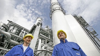 Zwei Werksmitarbeiter der BASF stehen vor einem Kraftwerk auf dem BASF-Betriebsgelände in Ludwigshafen. Hier will das Chemieunternehmen bis Ende 2026 rund eine Milliarde Euro einsparen.