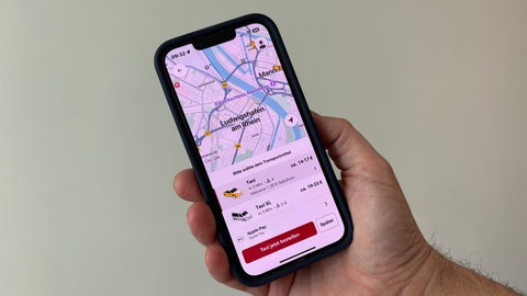 Eine Hand hält ein Handy mit einer Taxi-App drauf. Nutzer können in Ludwigshafen Taxis per App bestellen.