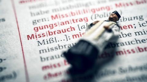 Miniaturfigur eines Priesters in einem Wörterbuch mit dem Wort Missbrauch. Symbolfoto. Zwei Jahre nach Beginn der Untersuchung gibt die Uni Mannheim erstmals Einblick in ihre Studie zu Missbrauchsfällen im Bistum Speyer.