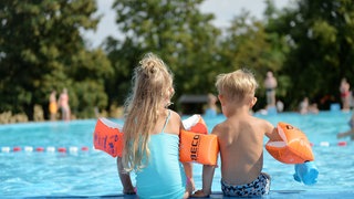 Zwei Kinder vor einem Schwimmbecken, die Sparvariante von Sommerurlaub. Urlaub mit Kindern ist für viele nicht möglich, weil er zu teuer ist