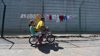 Kinder im August 2015 fahren in der Aufnahmeeinrichtung für Asylbegehrende in Ingelheim Fahrrad (Archiv) - Symbolbild: Landauer Flüchtlingshelferin: "Vieles haben wir nach zehn Jahren noch nicht geschafft."