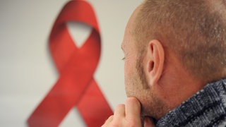 Welt-Aids-Tag 2025: (Symbolbild):  Ein Mann betrachtet nachdenklich eine große große Aids-Schleife.